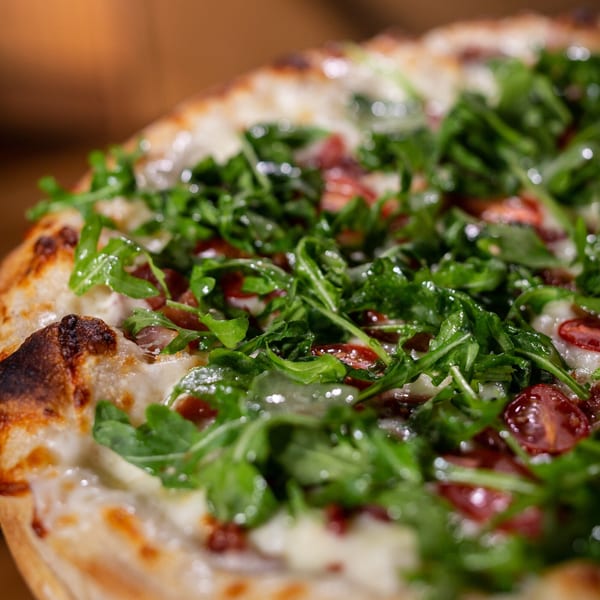 Close-up of a Halftime Pizza with fresh arugula, white cheese, and red toppings.