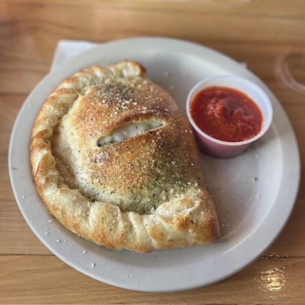 A golden-brown calzone, sprinkled with herbs and cheese, served with a side of marinara sauce.