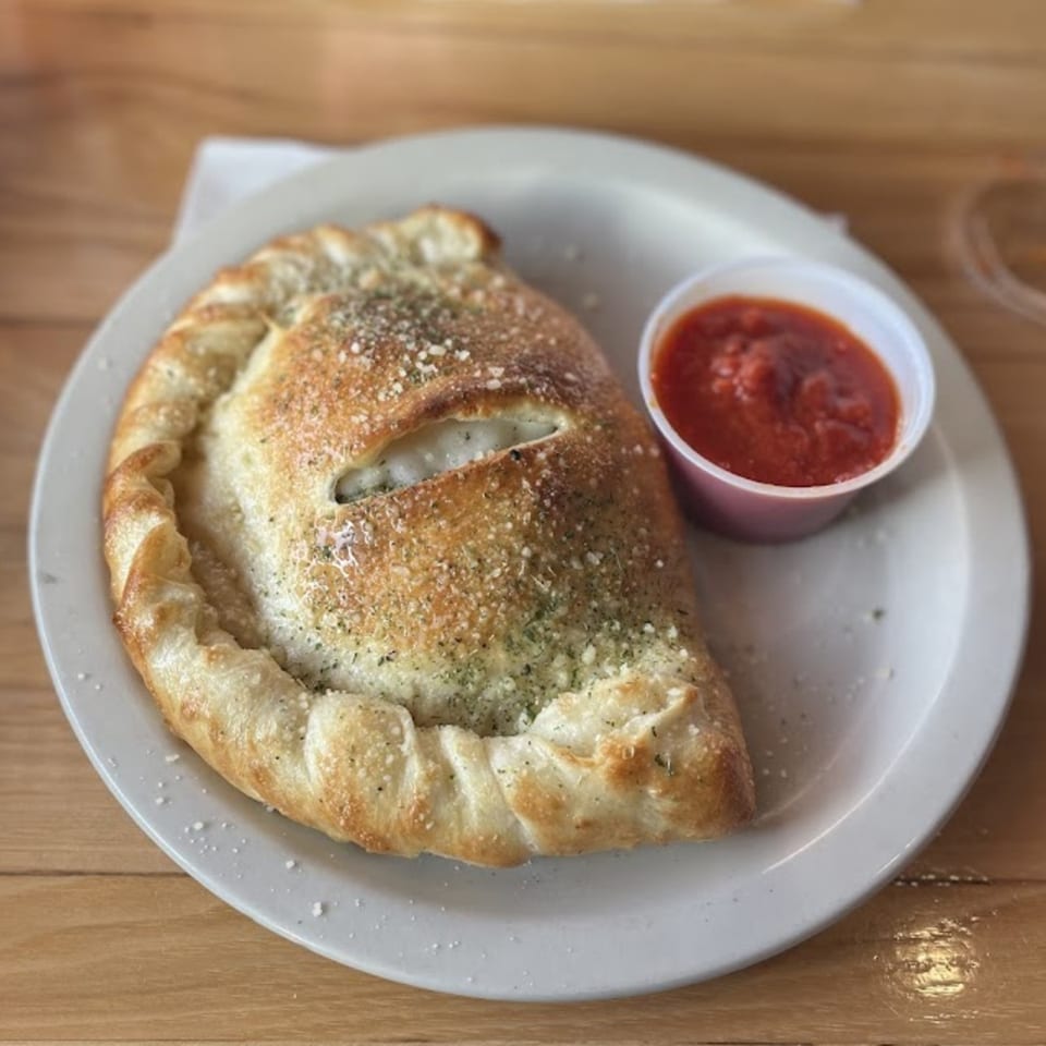 A golden-brown calzone, sprinkled with herbs and cheese, served with a side of marinara sauce.