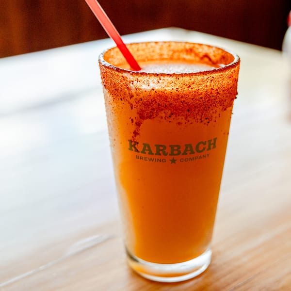 A Karbach Brewing Company glass filled with an orange drink, rimmed with chili powder, and a red straw.