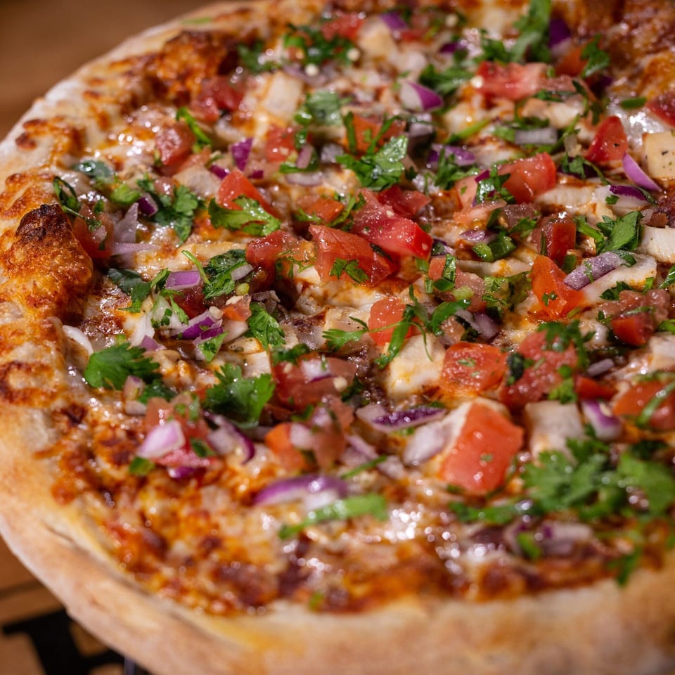 Halftime Pizza's chicken pizza, topped with diced tomatoes, red onions, and fresh cilantro.