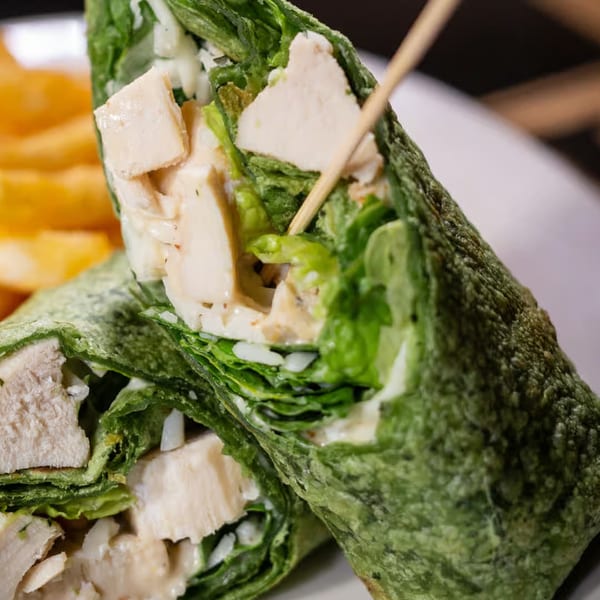 Close-up of a chicken Caesar wrap cut in half, revealing chicken, lettuce, and dressing.
