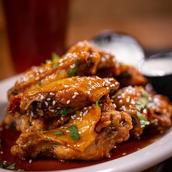 Halftime Pizza's glazed chicken wings, garnished with sesame seeds and cilantro, served with dipping sauce.