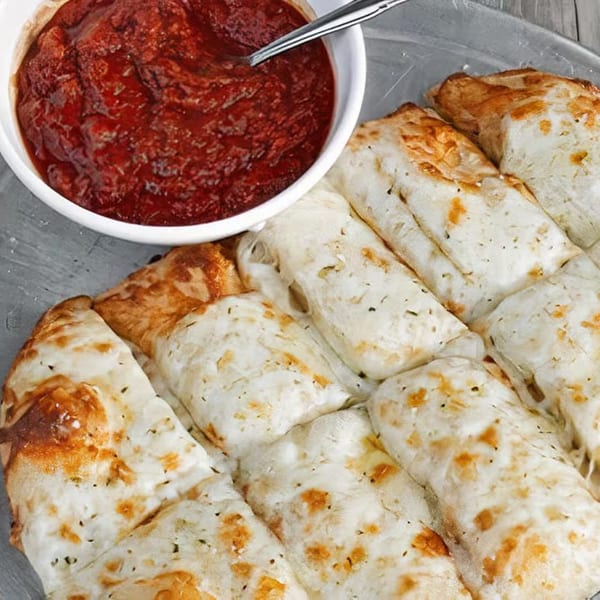 Halftime Pizza's cheesy breadsticks with herbs, served with a side of marinara sauce.
